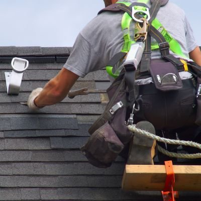 Roof repair expert fixing shingle damage with safety gear